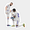 two soccer players in white uniforms with one kneeling down and the other standing on his knees